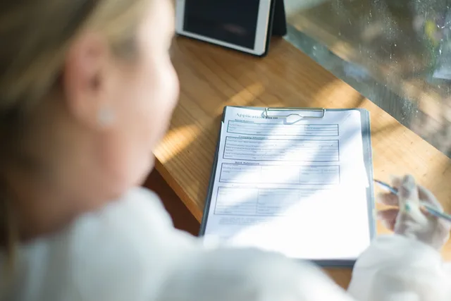 A woman fills out an application form with a pen at a sunlit wooden desk. Women founder funding strategy mistakes that keep a stalled route alive