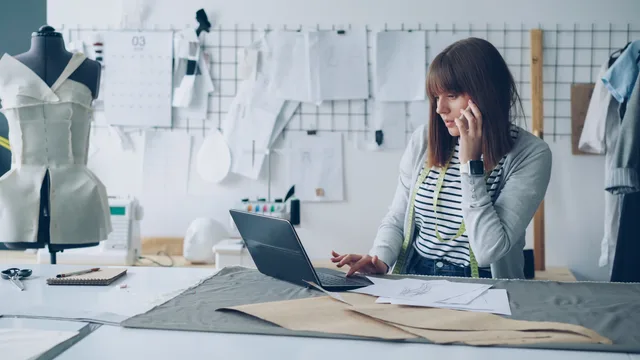 A female fashion designer working on her laptop in a creative design studio, surrounded by design sketches. Defining a women founder funding audience by funding job rather than stereotype